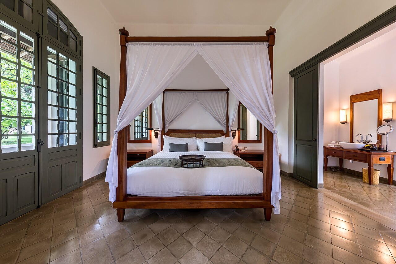 A canopy bed with white drapes beside tall shuttered doors